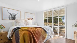 Ein Schlafzimmer mit einem großen Bett, zwei gerahmten Tierbildern, einem Nachttisch aus Holz und Blick auf einen Außenbereich durch eine Schiebetür.
