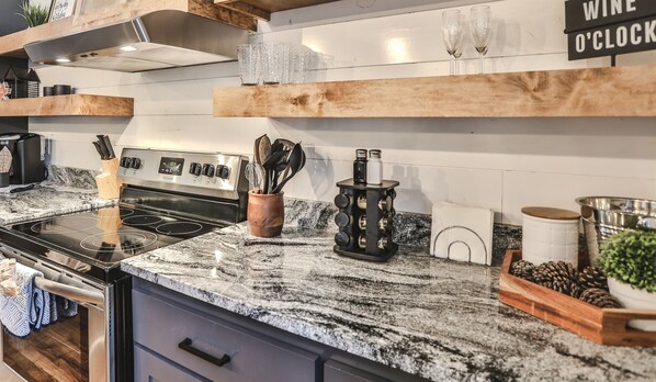 A kitchen with a granite countertop, stainless steel appliances, wooden shelves, and a sign that reads "WINE O'CLOCK".
