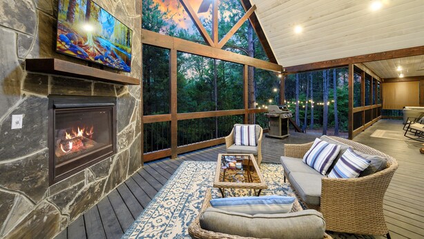A cozy outdoor living area with a stone fireplace, comfortable seating, and a large TV screen. - Top % Secluded 1.25ac: Spa Bath, Tub & Pull-Thru (Broken Bow)