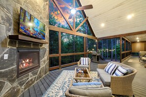 A cozy outdoor living area with a stone fireplace, comfortable seating, and a large TV screen.