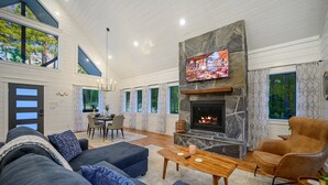 A spacious living room with a fireplace, a television mounted above it, and a dining area with a table and chairs. - Top % Secluded 1.25ac: Spa Bath, Tub & Pull-Thru (Broken Bow)