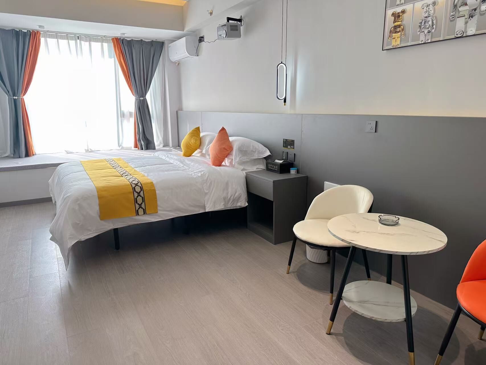 Habitación de hotel con cama, mesita de noche, dos sillas, una mesita pequeña y una ventana con cortinas.