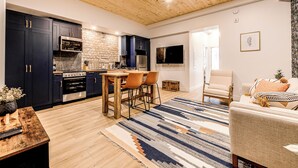 A modern kitchen with dark cabinets, a wooden ceiling, and a dining area with a striped rug. - Historic Two Bedroom Facing Parliament (Québec)