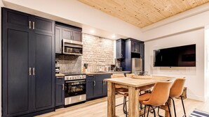 A modern kitchen with dark cabinets, a stone backsplash, and a wooden ceiling. - Historic Two Bedroom Facing Parliament (Québec)