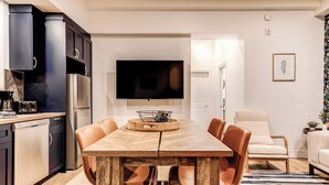 A modern kitchen with dark cabinets, a stainless steel refrigerator, and a flat-screen TV mounted above the dining table. - Historic Two Bedroom Facing Parliament (Québec)