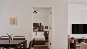 A modern hotel room with a wooden floor, a dining area with a table and chairs, a bed with a headboard, a TV mounted on the wall, and a bookshelf. - Mint House Washington DC Downtown by Kasa (Washington)