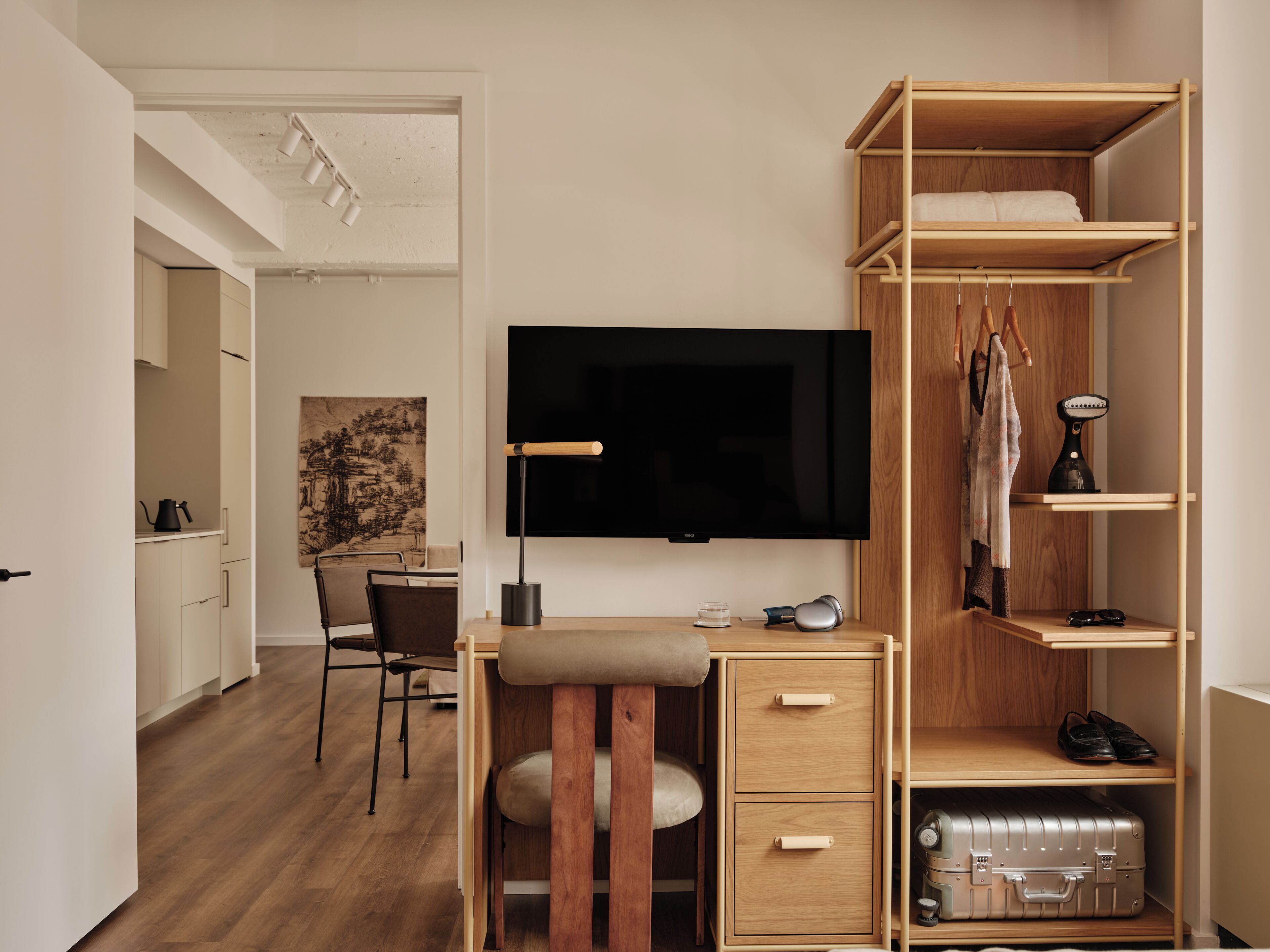 A modern bedroom with a wooden desk, a flat-screen TV, a wardrobe, and a suitcase.