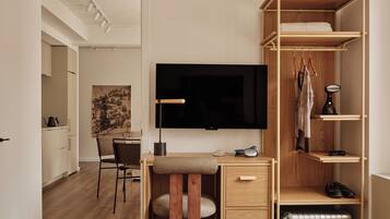 A modern bedroom with a wooden desk, a flat-screen TV, a wardrobe, and a suitcase.