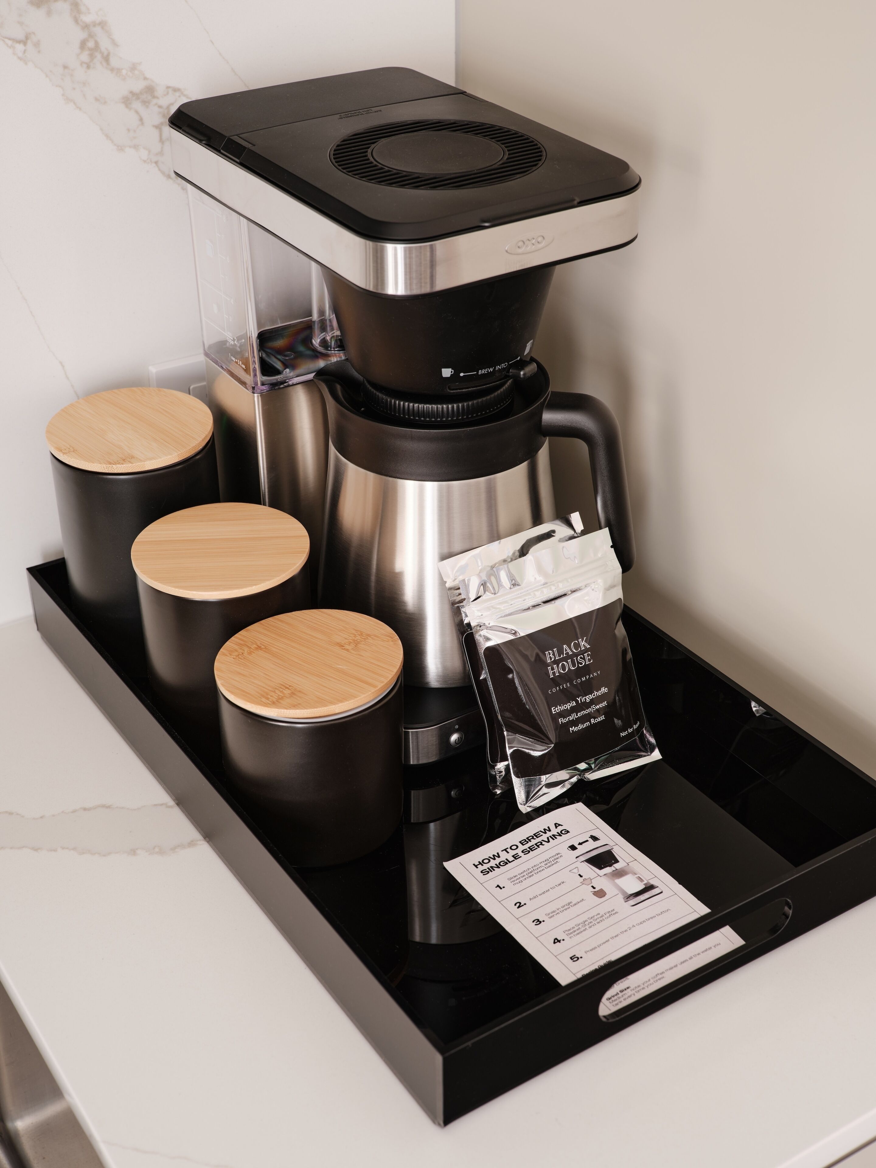 A coffee maker with four wooden containers and a coffee bag on a black tray.