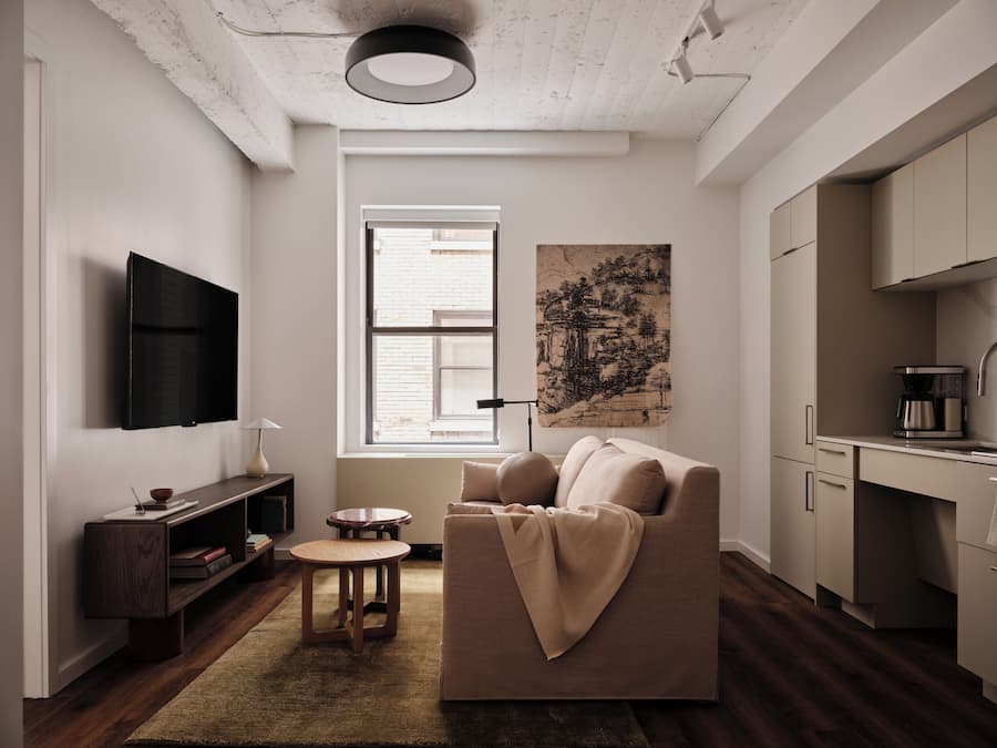 Ein modernes Wohnzimmer mit Sofa, Couchtisch, Fernseher und Küchenzeile mit Schränken und einer Kaffeemaschine.