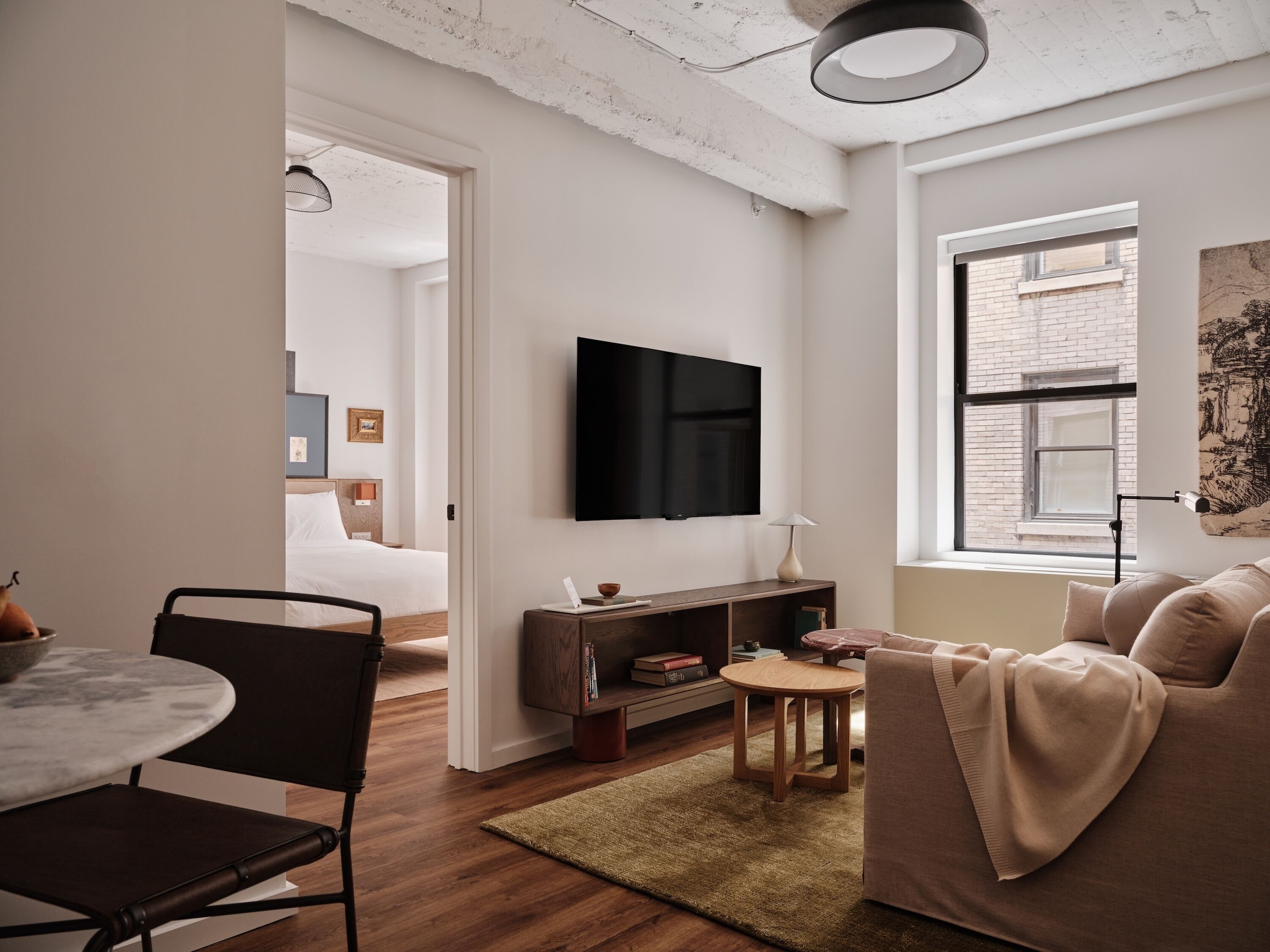 A modern living room with a flat-screen TV, a sofa, a coffee table, and a dining area with a chair and a small table.