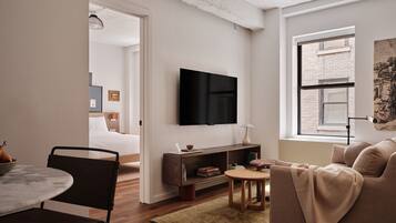 A modern living room with a flat-screen TV, a sofa, a coffee table, and a dining area with a chair and a small table.