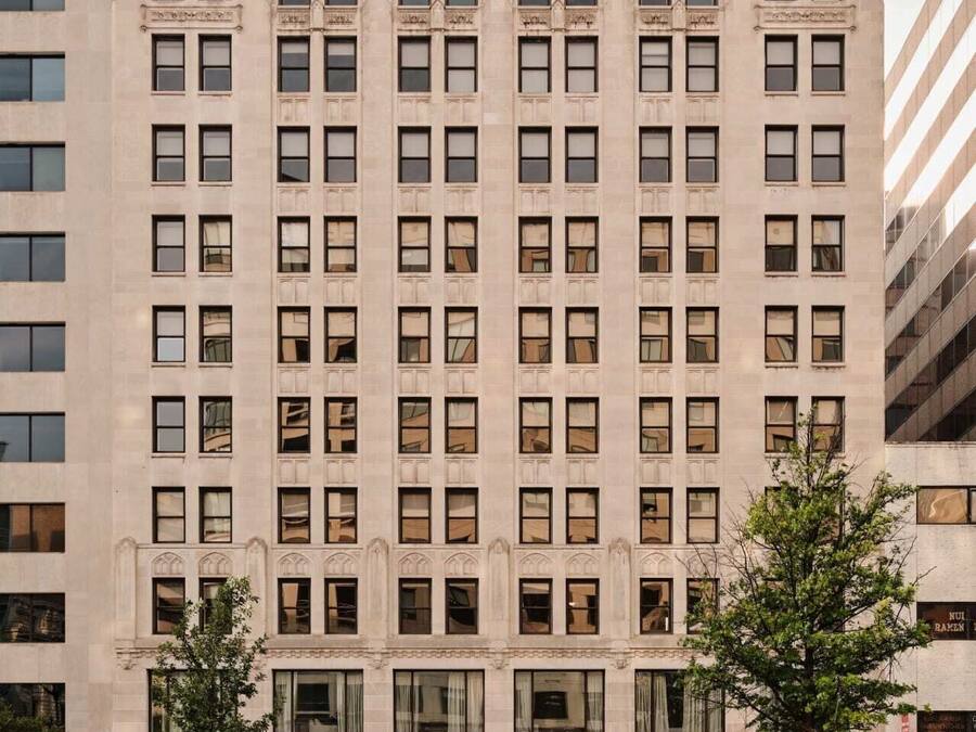 Un edificio de varios pisos con fachada simétrica, ventanas regularmente espaciadas y detalles decorativos alrededor de las mismas.