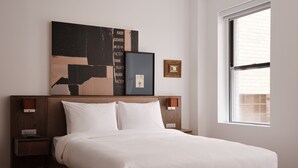 A neatly made bed with white linens in a modern room with a wooden headboard, a large abstract painting above the bed, and a window with blinds. - Mint House Washington DC Downtown by Kasa (Washington)