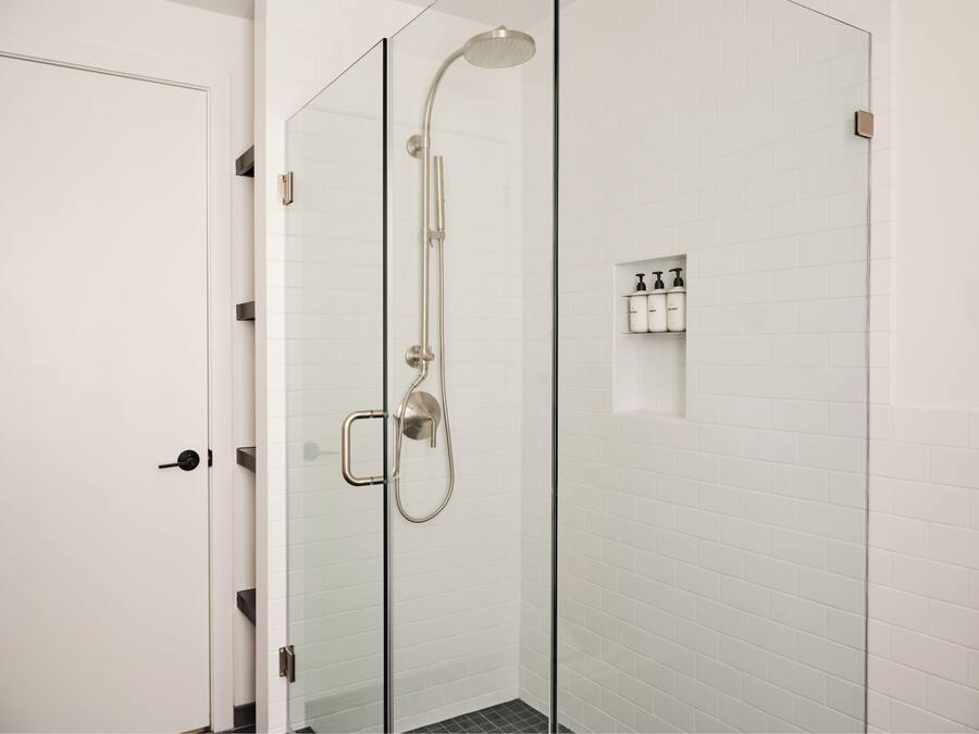 A modern shower with a glass door, a handheld showerhead, and a wall-mounted control panel.