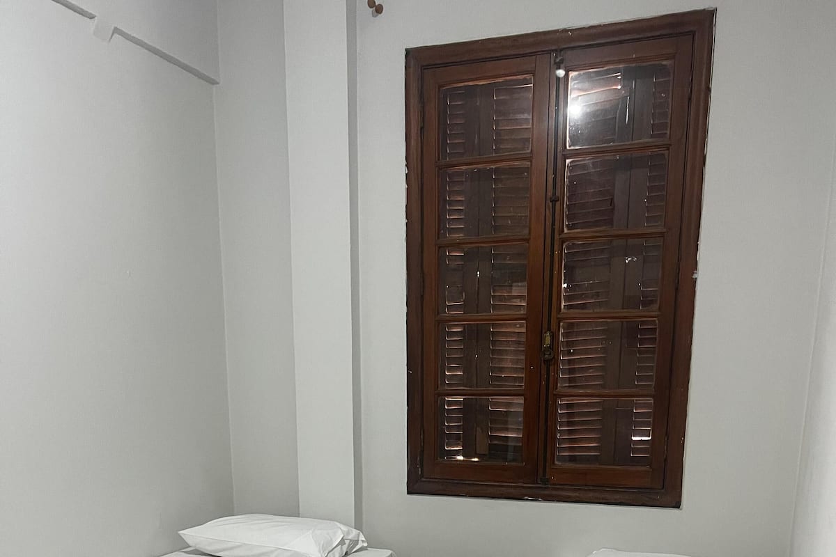 A small, clean room with two single beds, a wooden floor, and a window with wooden shutters.