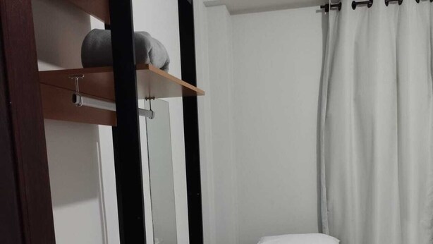 A small, single-bed room with a wooden shelf above the bed, a white curtain, and a door with a metal handle. - Hotel Rodoviária Belo Horizonte (Belo Horizonte)