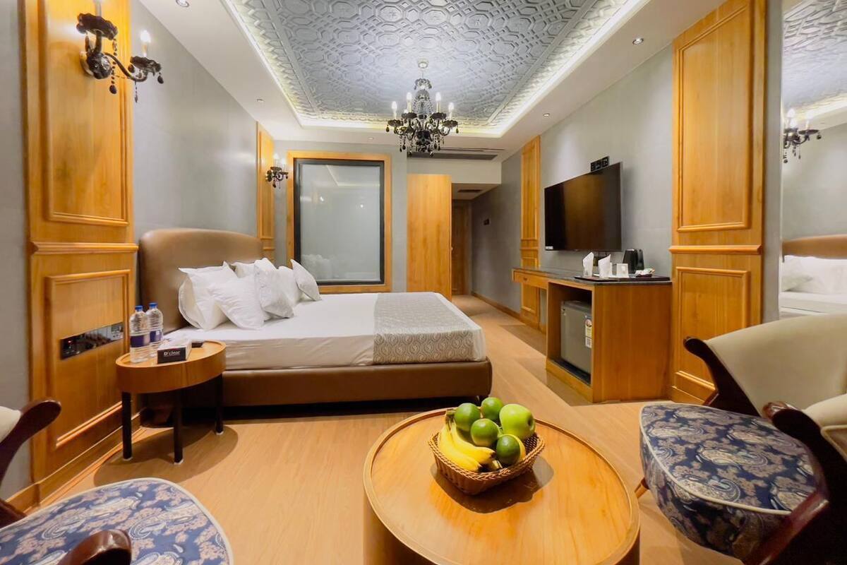 A hotel room with a bed, a TV, a desk, and a dining table with fruit.