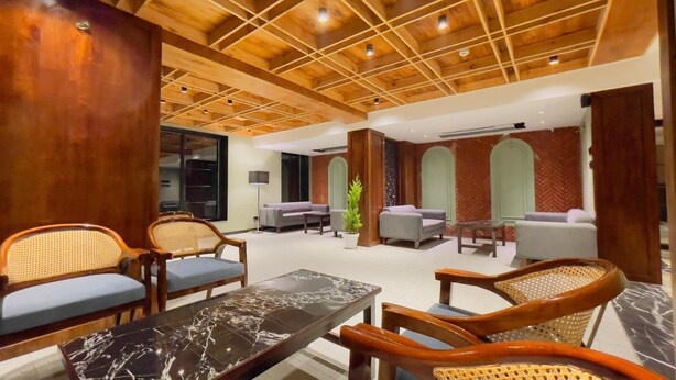 A spacious lobby with wooden ceiling beams, seating areas with cushioned chairs and sofas, and a marble-topped table. - Paradise Premium (Srinagar)