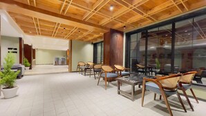 A spacious lobby with wooden ceiling beams, a seating area with chairs and tables, and a large glass wall providing a view of the interior. - Paradise Premium (Srinagar)