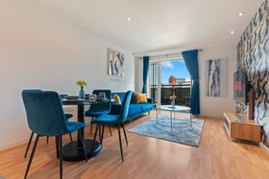 Un salon moderne avec un canapé bleu, une table à manger et des chaises, et un téléviseur fixé au mur.