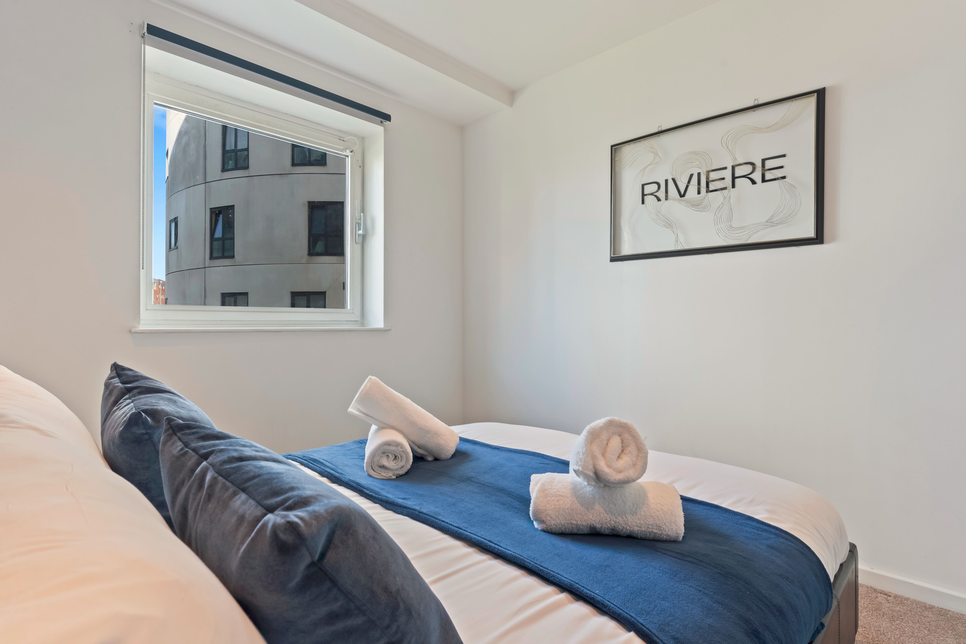 A hotel room with a bed, a window, and a framed sign on the wall.