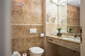 A bathroom with a toilet, sink, and mirror. There are towels and a plant on the counter.