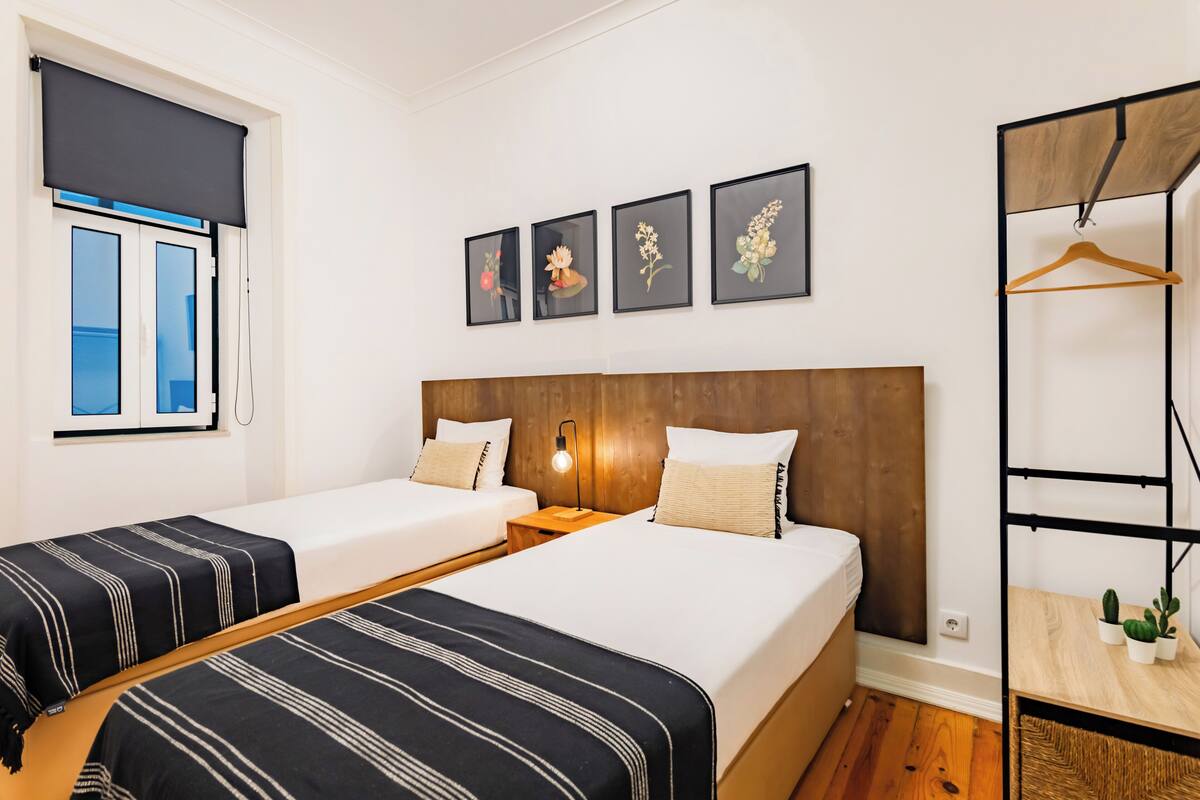 Ein Hotelzimmer mit zwei Betten, einem Holzkopfstück, einer Wandleuchte und einem Fenster mit Jalousie.