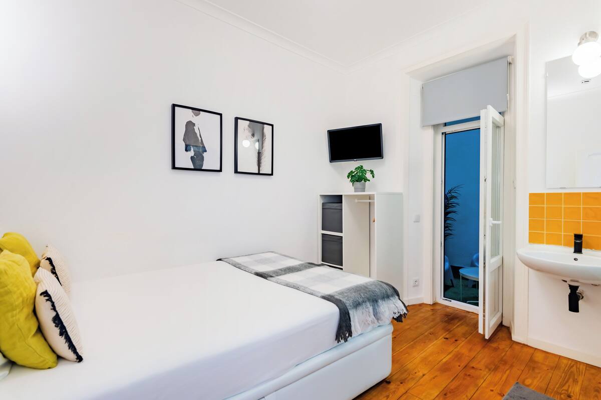 Ein Schlafzimmer mit Bett, Fernseher, Pflanze und einem Badezimmer inklusive Waschbecken.