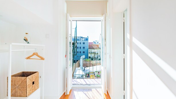 Ein schmaler Korridor mit Holzboden führt zu einem Balkon mit Blick auf Gebäude.