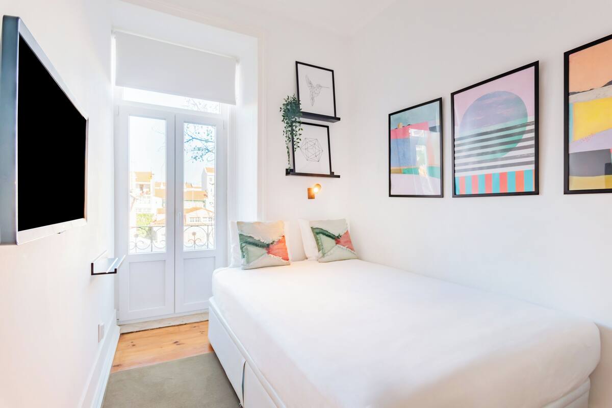 Ein Schlafzimmer mit Bett, einem an der Wand montierten Fernseher und gerahmten Bildern.