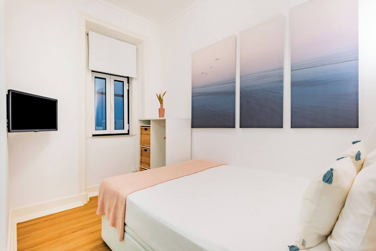 Ein Schlafzimmer mit Bett, Fernseher, Fenster und Wandbildern.