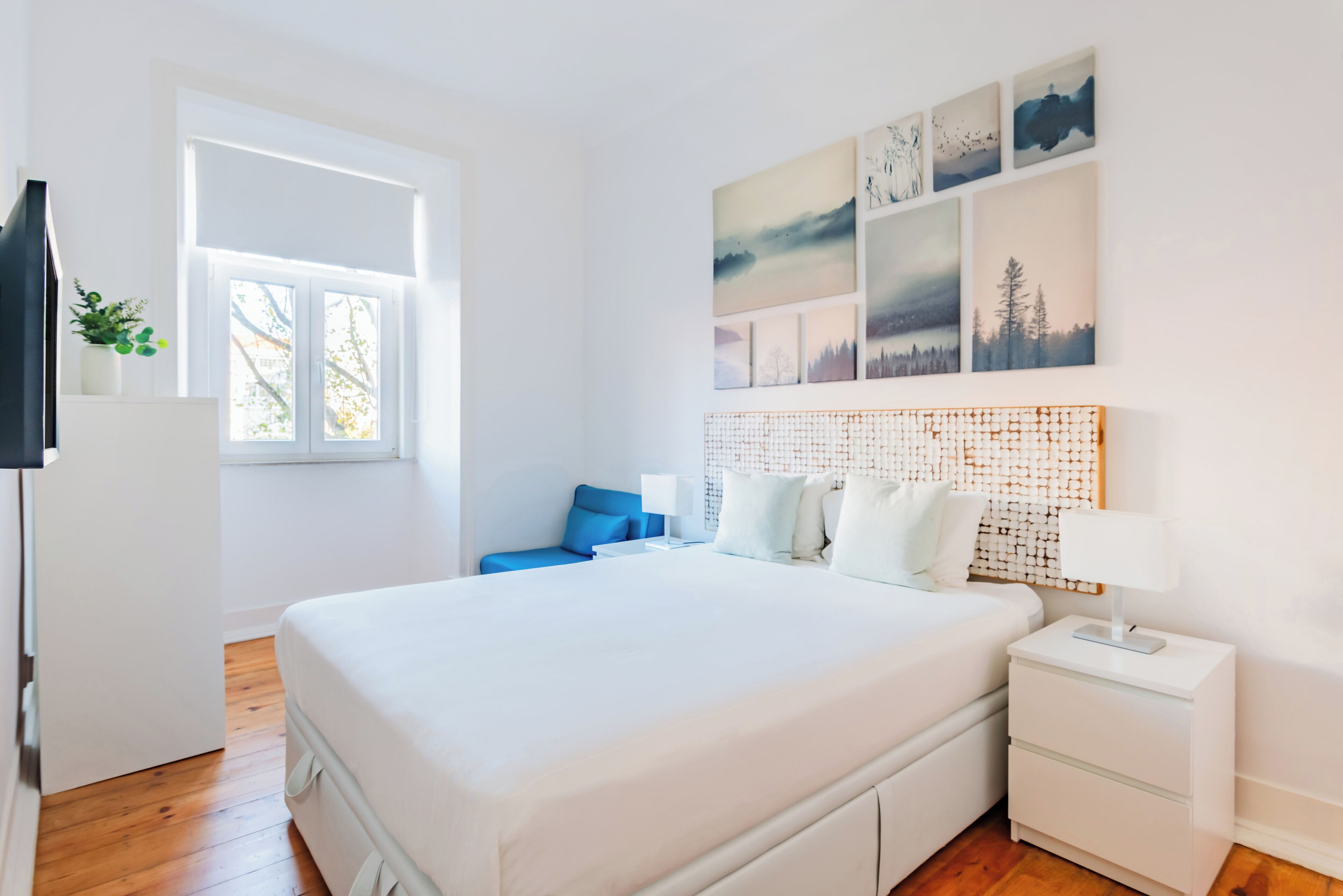 Une chambre moderne avec un grand lit, une table de chevet, une commode, une fenêtre et un mur décoré d’œuvres d’art.