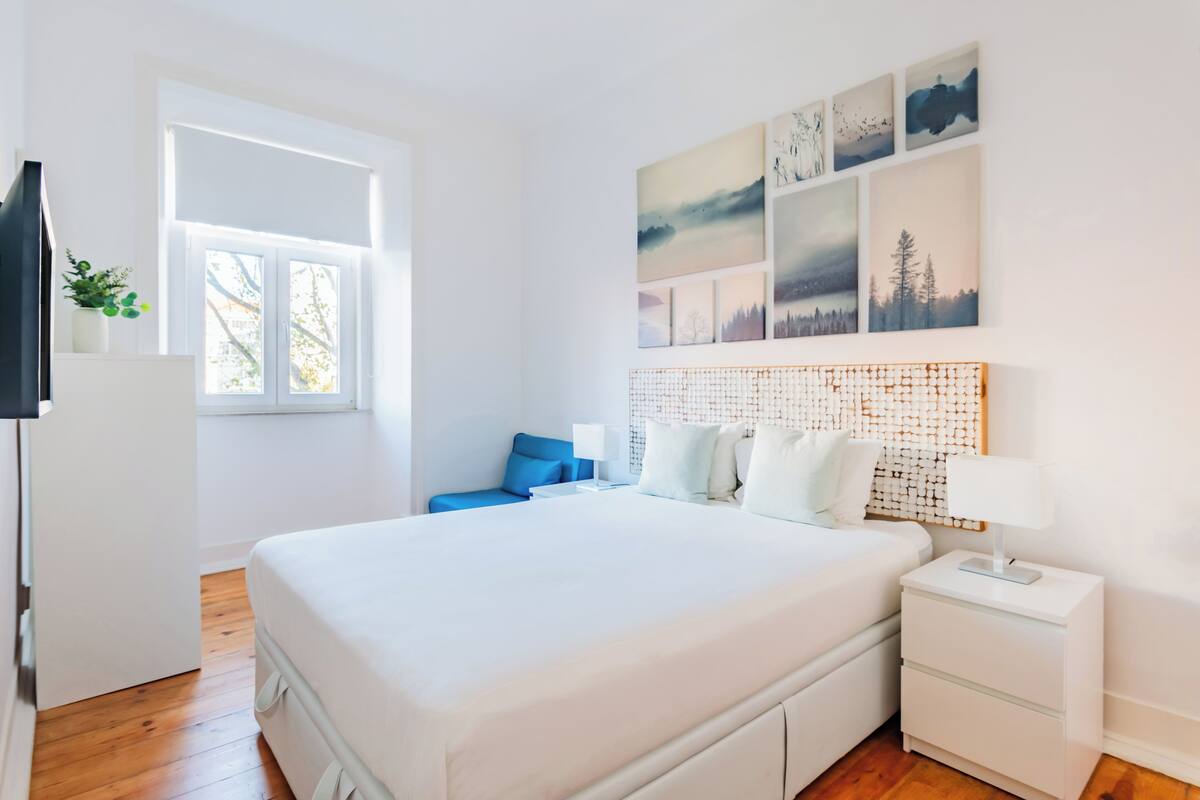 Ein modernes Schlafzimmer mit einem großen Bett, einem Nachttisch, einem Beistelltisch, einem Fenster und Wandbildern.