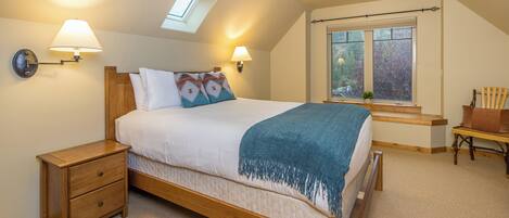Un dormitorio con cama de madera, dos mesitas de noche, un tragaluz y una ventana.