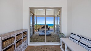 A room with a view of the ocean through a glass door, wicker baskets on shelves, and a white bench with patterned cushions. - Berry's Beach Retreat Ventnor Phillip Island (Ventnor)