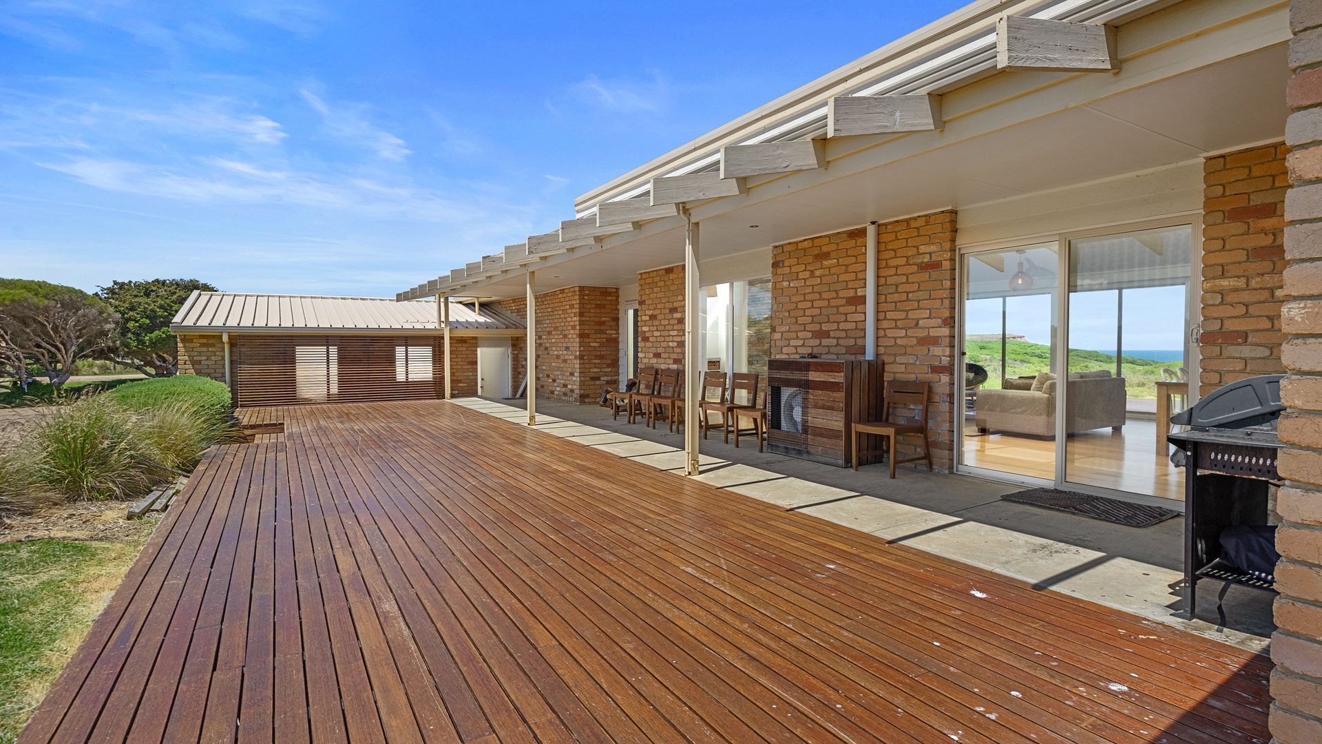 A modern house with a wooden deck, brick walls, and large glass doors leading to an outdoor seating area.