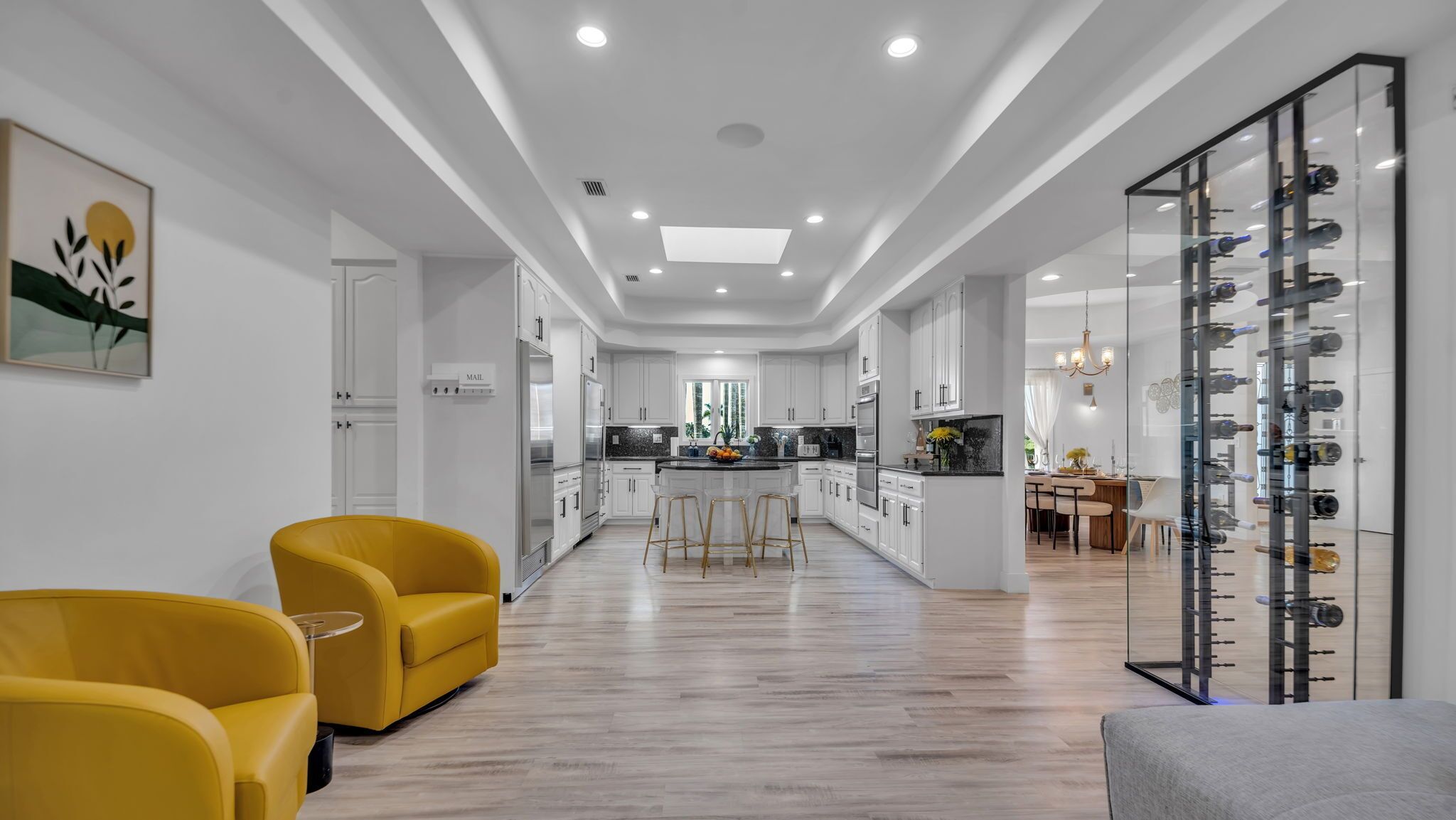 Une cuisine moderne avec des meubles blancs, un îlot central et un coin repas doté de chaises jaunes.