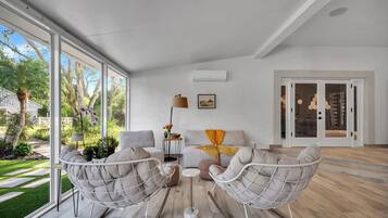 Un salon moderne doté d’une grande porte vitrée donnant sur un jardin, d’un ensemble de canapés et d’un lampadaire.