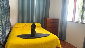 A room with a wooden bed, yellow bedding, a wooden dresser, and a window with curtains.