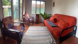 A room with a sofa, two chairs, a small table, and a potted plant.