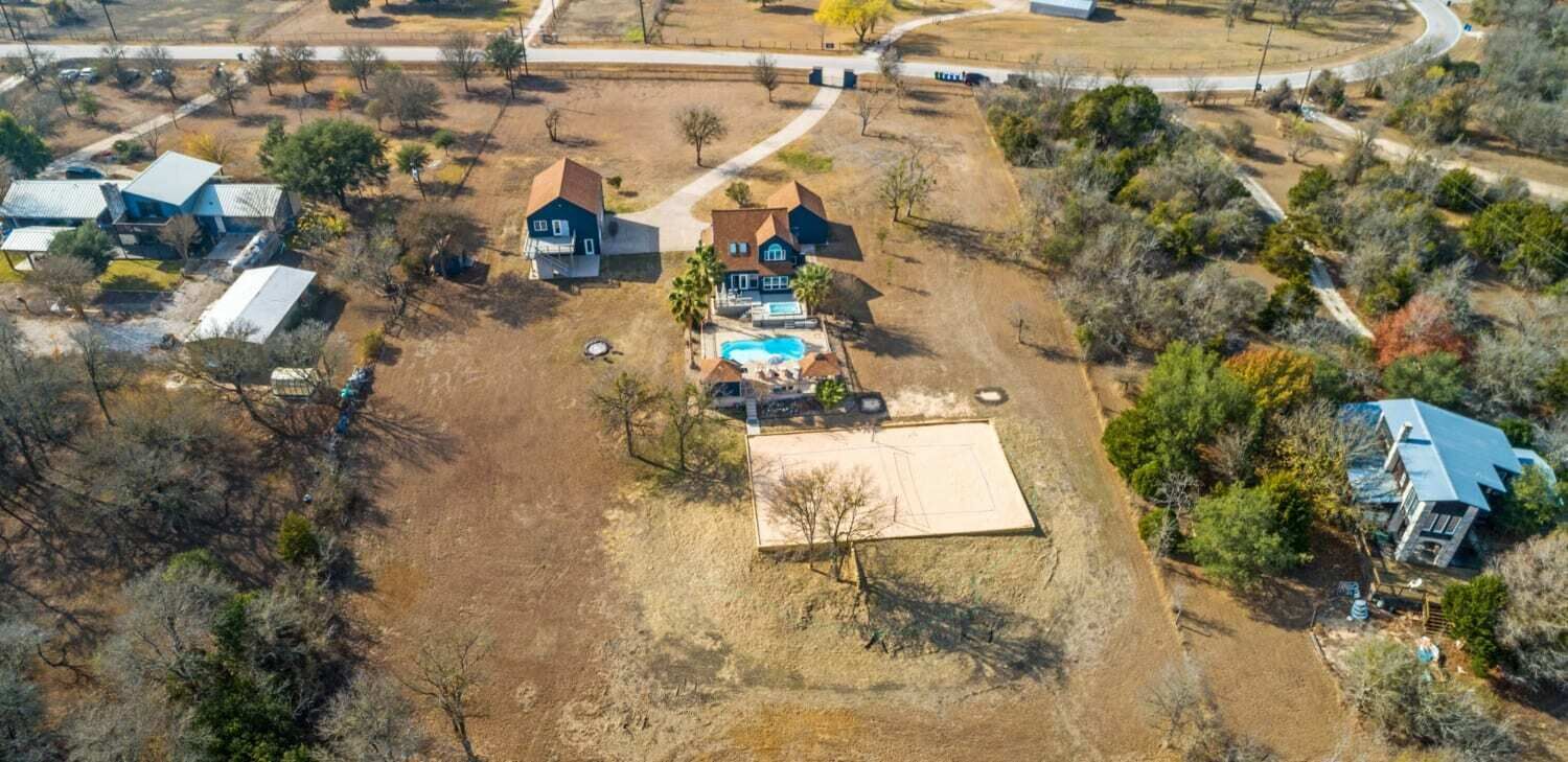 An aerial view of a residential area with multiple houses, a swimming pool, and a large open field.