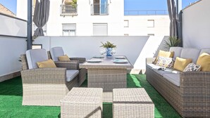 Une terrasse extérieure avec des meubles en osier, une table dressée pour le repas et, en arrière-plan, la vue d’un bâtiment.