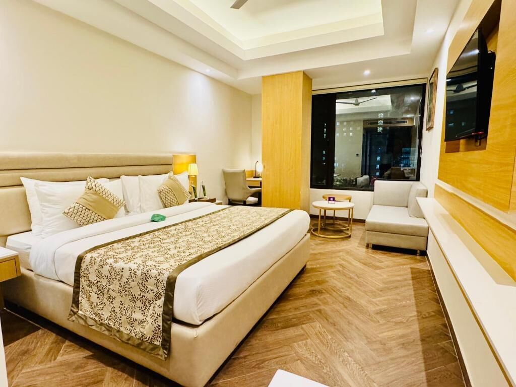 A hotel room with a bed, a small table, a chair, a sofa, and a large window.