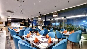 A restaurant with blue chairs, tables set with orange napkins, and a view of the city at night. - Click collection Lucknow (Lucknow)