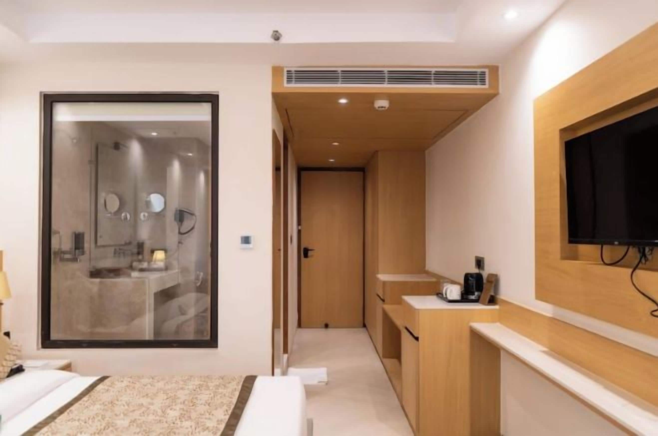 A hotel room with a bed, a bathroom with a mirror, a TV mounted on the wall, and a wooden cabinet.