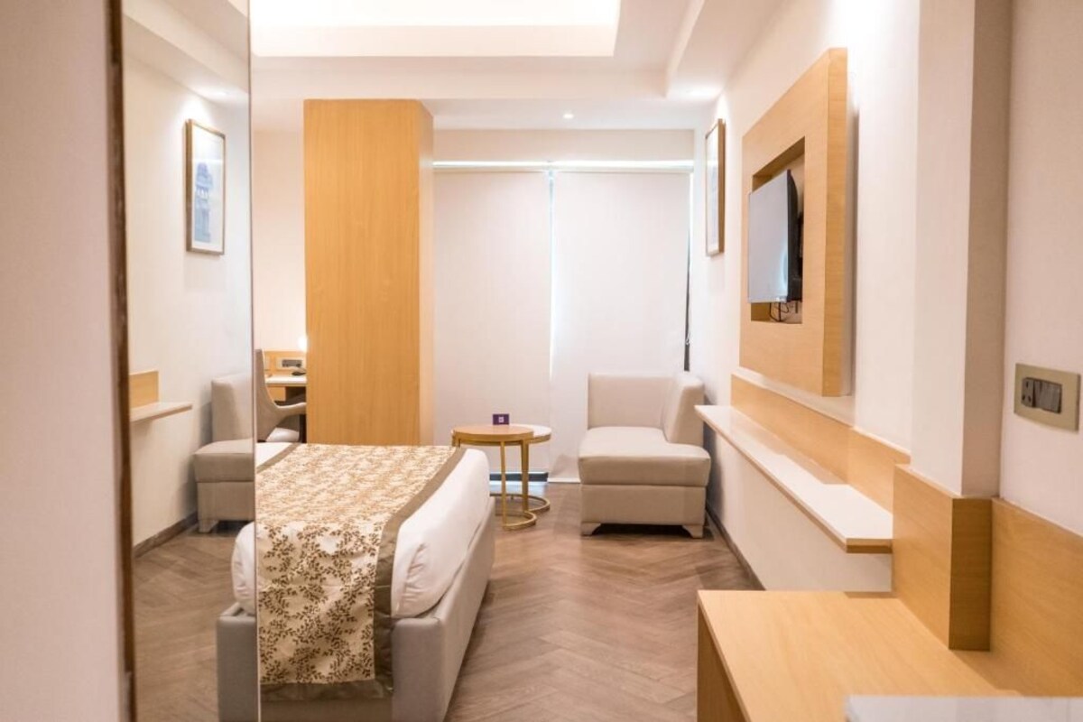 Une chambre d’hôtel équipée d’un lit, d’un bureau, d’une chaise, d’une petite table et d’un téléviseur fixé au mur.