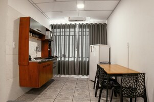 Una cocina compacta con un mueble de madera, un refrigerador, una mesa de comedor con sillas y una cortina.
