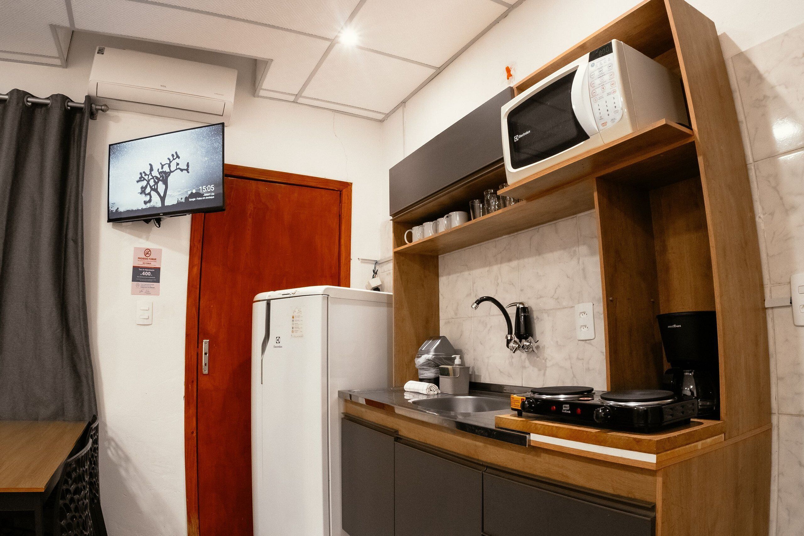 Una cocina compacta equipada con microondas, cafetera y un televisor montado en la pared.