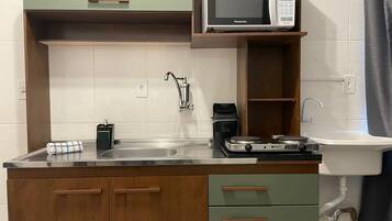 Una cocina compacta con microondas, cafetera y lavabo.